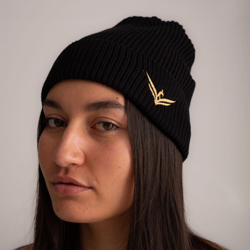 Black beanie hat with gold embroidered wild warrior wings logo, front view.