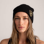 Black beanie hat with embroidered wild warrior badge logo, front view.