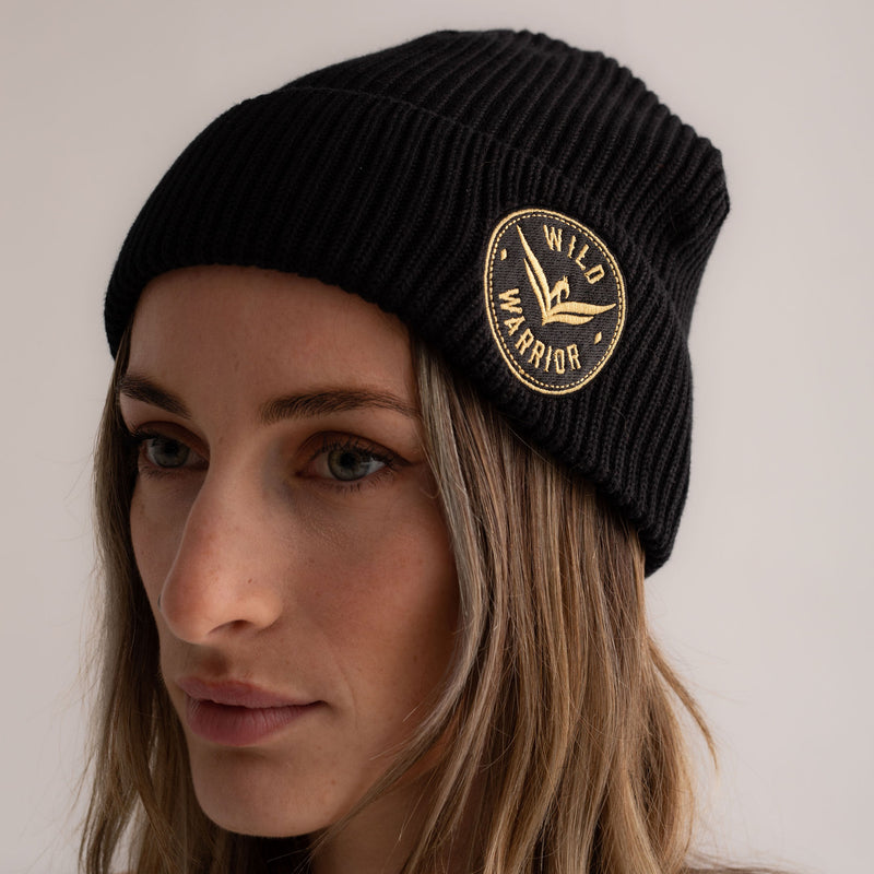 Black beanie hat with embroidered wild warrior badge logo, front view.