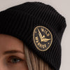 Black beanie hat with embroidered wild warrior badge logo, close-up embroidery.