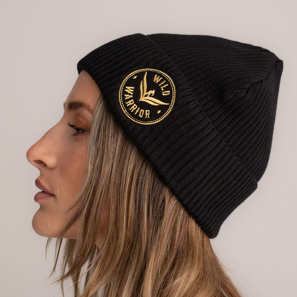Black beanie hat with embroidered wild warrior badge logo, side view.