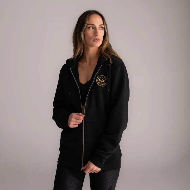 Wild Warrior Style Woman wearing black zip up hoodie with Wild warrior gold logo badge embroidered on front left side 
