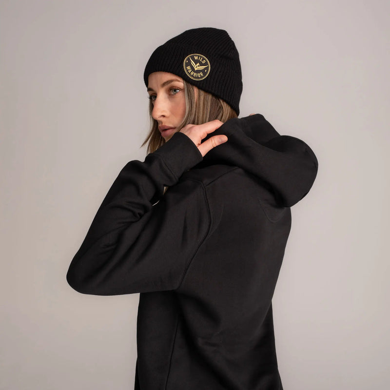 woman wearing black hoodie and black beanie with gold wild warrior badge embroidered